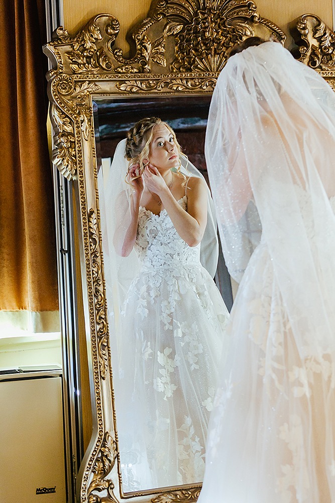 Winter wedding bride with mirror putting her earrings on in front of human size golden mirrow Montebello photographers Eva Hadhazy