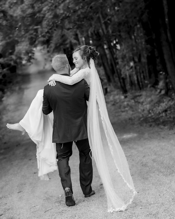 Groom carrying bride down a forest path at an intimate micro wedding