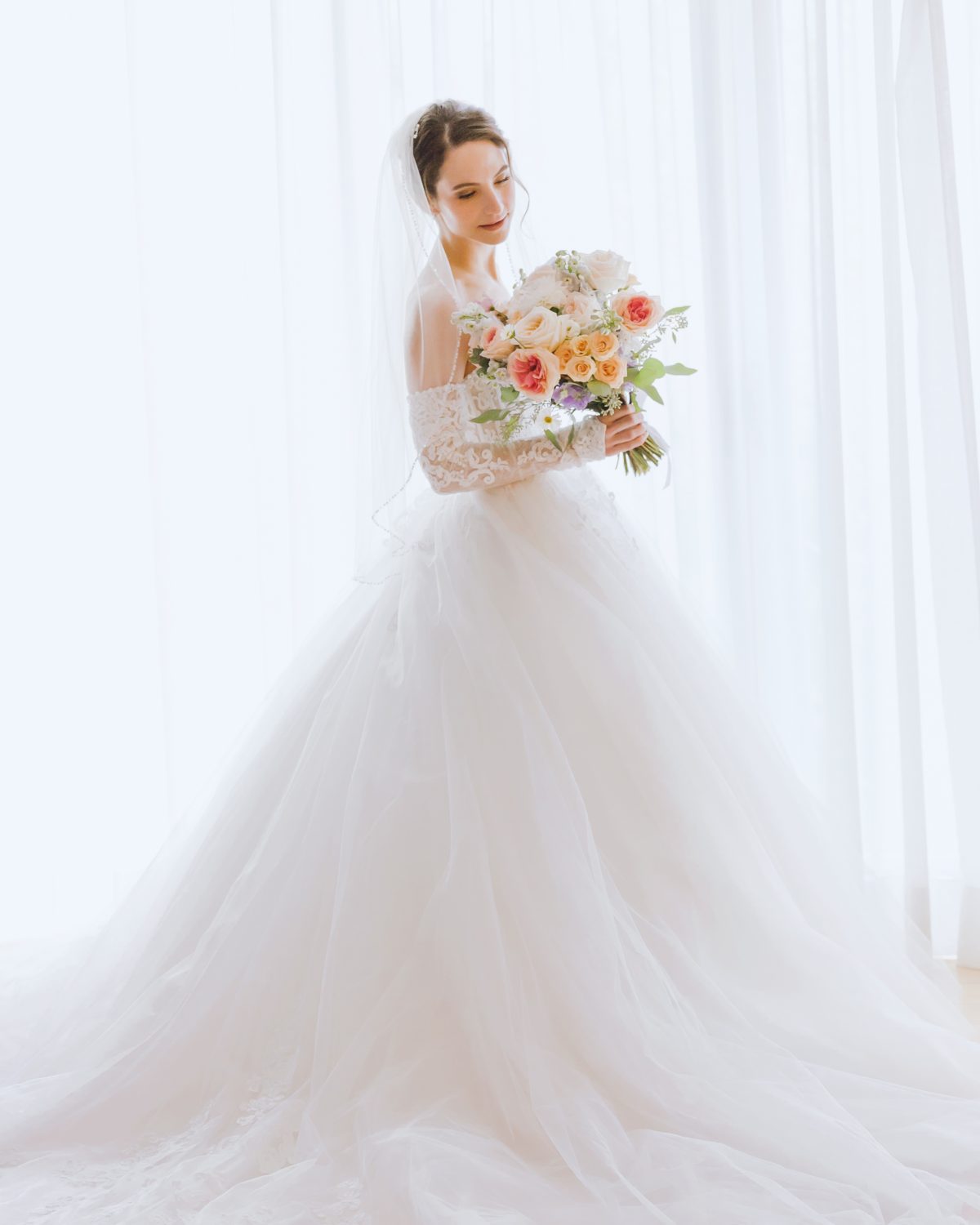 bride is smelling and looking at flower bouque against the white backdrop editorial style