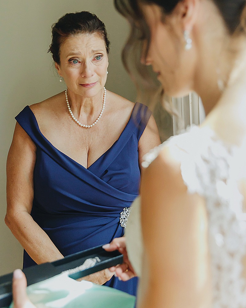 mom is looking at bride with tear in her eyes as the bride is opening up her present from mom