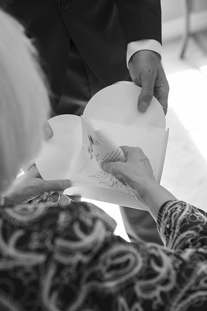 Grainy black and whote of shot from behind mom who is lifint her present from her son, a haeart shaped handkirschief .