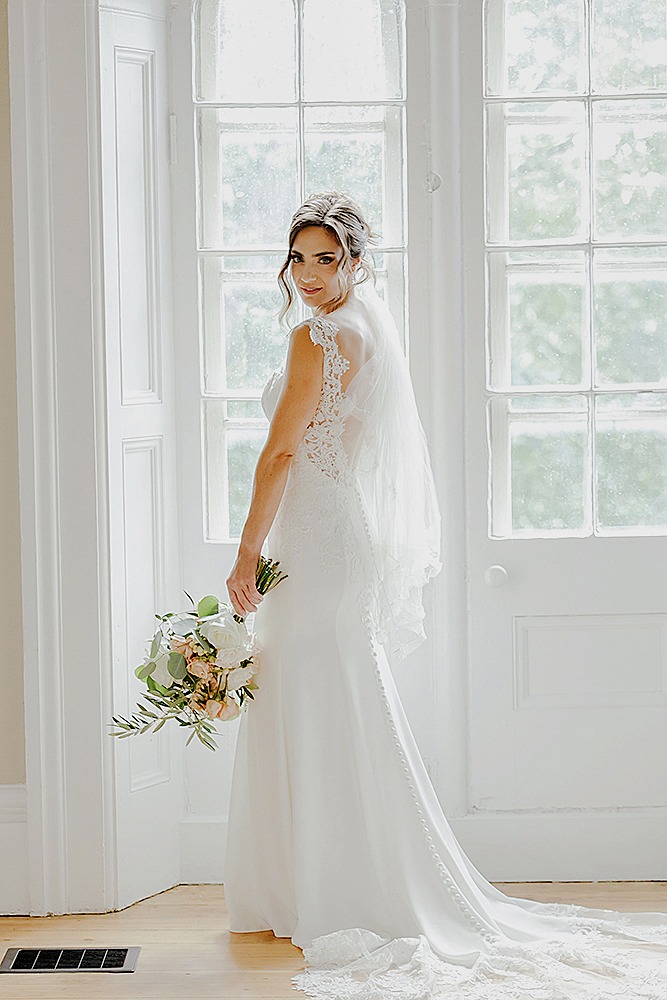 editorial photo of bride in front of large windows at farmhouse in strathmere bride body is halfway turned away looking back at camera
