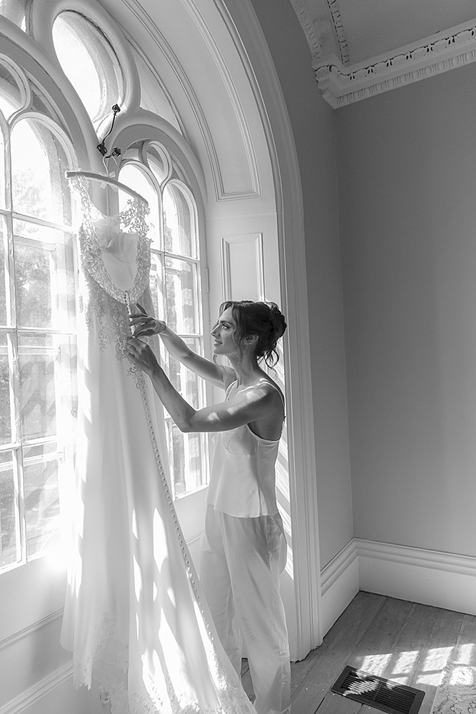 bride adjusting her dress that hangs from the windows inside the farmhouse