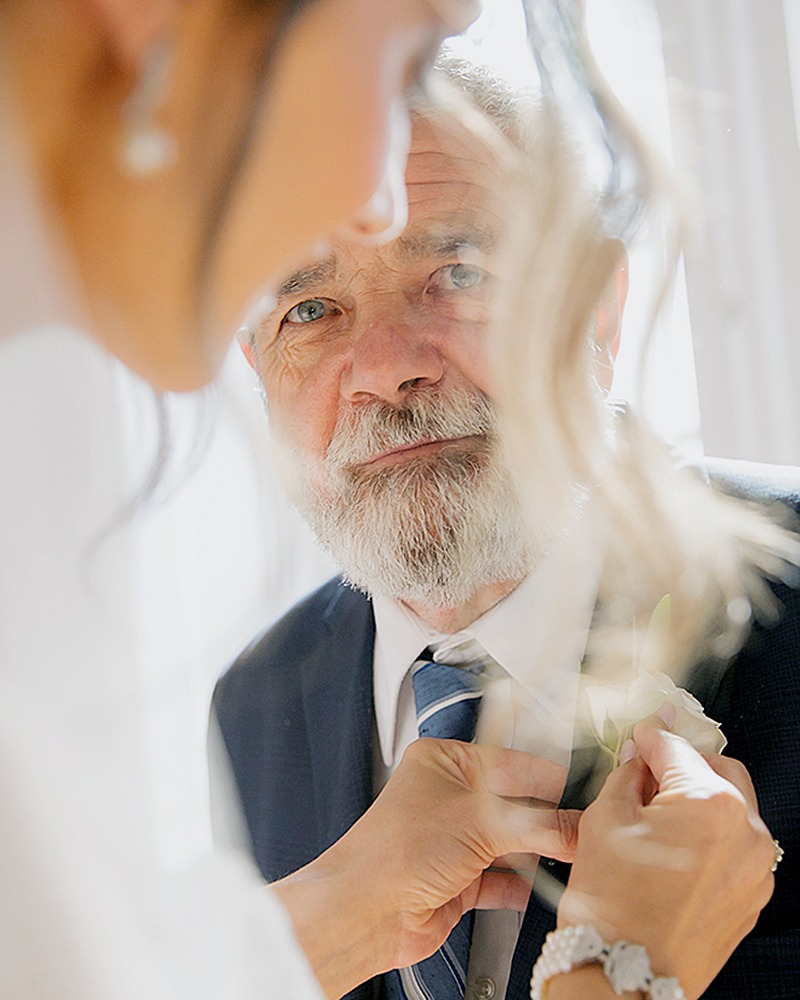 bride outting on the buttenier on dad, while dad look at bride with emotions