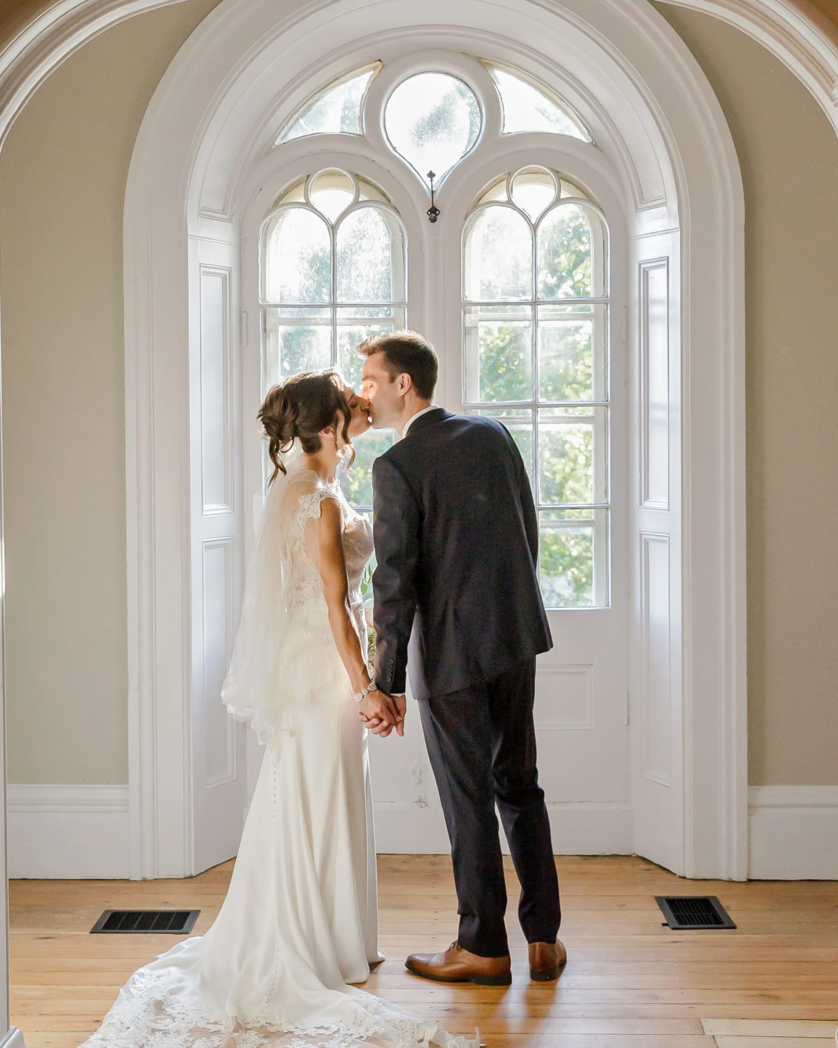 Wedding couple is kissing inside the Farmhouse at Strathemre. The light is falling on them through the large windows behind them.
