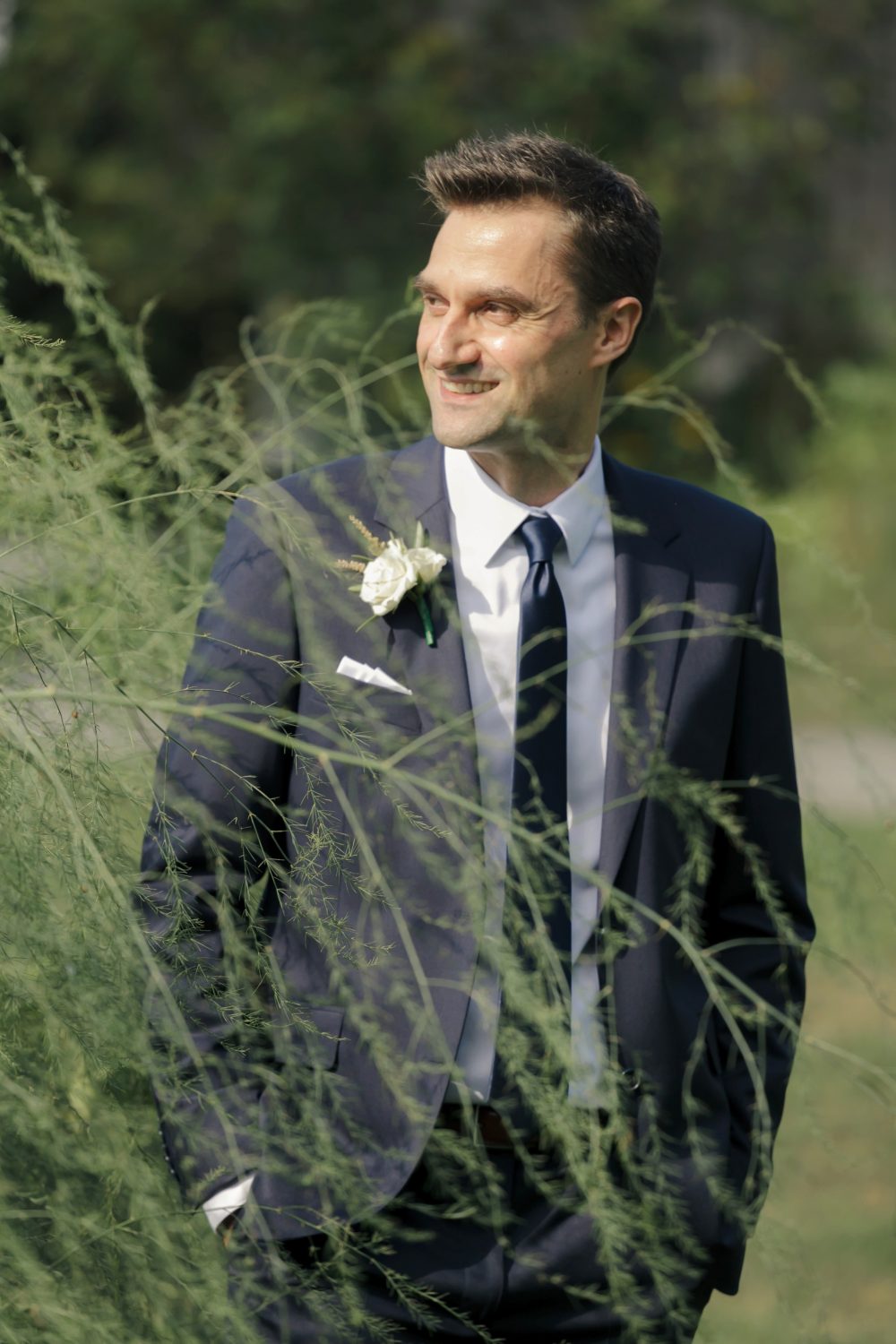 portrait of groom. his body is facing the sun slight grennery n front of him. editorial style