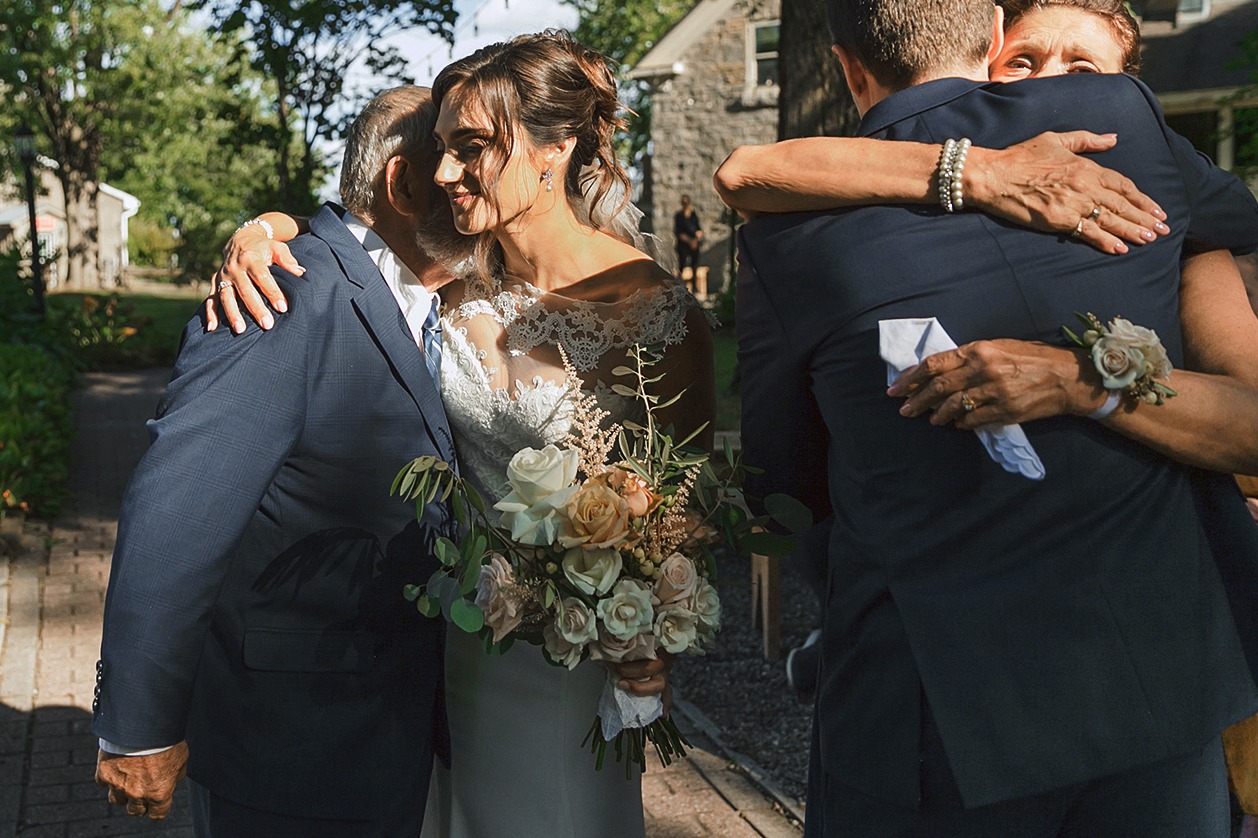 emotional hug between parents, bride and groom as parents give away bride to groom
